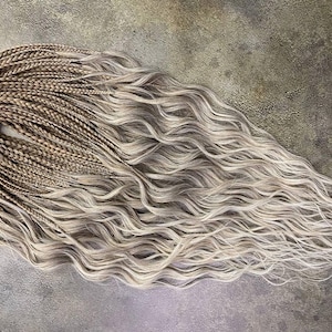 May include: Braided hair extensions in a blend of light brown and silver-gray tones. The braids transition into wavy, loose strands, creating a natural, textured look. The hair is bundled together at the top with a light-colored band.