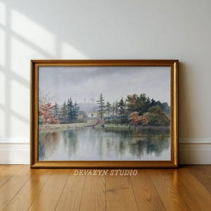 May include: A framed watercolor painting of a serene lake scene with trees and a bridge. The artwork is in a gold-colored frame and features a muted color palette of greens, browns, and grays. The text "DEVZAYN STUDIO" is at the bottom.