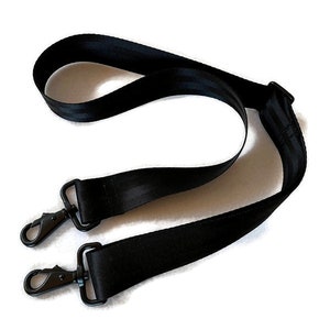 May include: Black adjustable shoulder strap with two metal clasps. The strap is made of a durable, woven material.