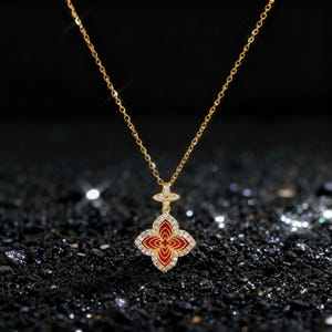 May include: A gold-colored necklace with a pendant featuring a red and white floral design. The pendant is encrusted with small, clear gemstones. The necklace chain is delicate and hangs against a dark, textured background.