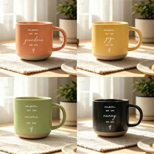 Puede incluir: Cuatro tazas de cer&aacute;mica en tonos naranja, amarillo, verde y negro. Cada taza tiene una base y un asa de color crema. Las tazas est&aacute;n inscritas con la palabra "mam&aacute;" y un t&eacute;rmino de cari&ntilde;o, junto con el a&ntilde;o de establecimiento y un s&iacute;mbolo de coraz&oacute;n.