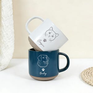 Puede incluir: Dos tazas de cer&aacute;mica, una blanca y otra verde azulado, apiladas. La taza blanca presenta una ilustraci&oacute;n de gato y el nombre "Cooper". La taza verde azulado tiene una ilustraci&oacute;n de perro y el nombre "Bailey". Ambas tazas tienen una base marr&oacute;n.