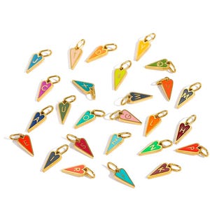 May include: A collection of gold-colored heart-shaped charms, each with a different letter in a contrasting color. The charms are arranged on a white surface. The letters are in various colors, including blue, green, and pink.