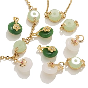 May include: A selection of gold-coloured necklaces and pendants with jade-like stones in green and white. The pendants have floral and circular designs. Some pendants are attached to delicate gold chains.