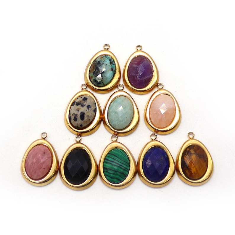 May include: A collection of teardrop-shaped pendants with various gemstones, including turquoise, amethyst, and tiger's eye. Each stone is set in a gold-colored bezel. The pendants are arranged on a white background.