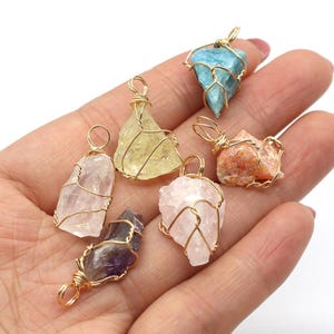 May include: A collection of gemstone pendants in various colors, including blue, yellow, pink, and orange. Each stone is wrapped in gold-colored wire, creating a unique and natural look. These pendants are ideal for jewelry making or as individual charms.