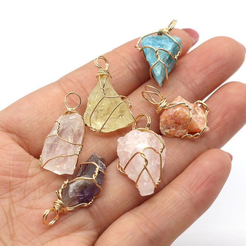 May include: A collection of gemstone pendants in various colors, including blue, yellow, pink, and orange. Each stone is wrapped in gold-colored wire, creating a unique and natural look. These pendants are ideal for jewelry making or as individual charms.