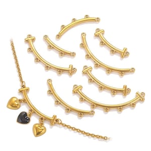 Puede incluir: Componentes de joyería dorados, que incluyen barras curvas con múltiples agujeros para conectar cuentas o dijes. También se muestra un collar con corazones dorados y un dije de corazón negro.