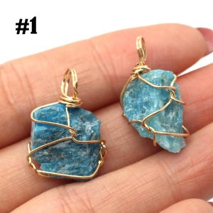 May include: Two raw, light blue apatite crystal pendants wrapped in gold-colored wire. The pendants are irregularly shaped and have a natural, textured appearance. The number "#1" is visible in the upper left corner.