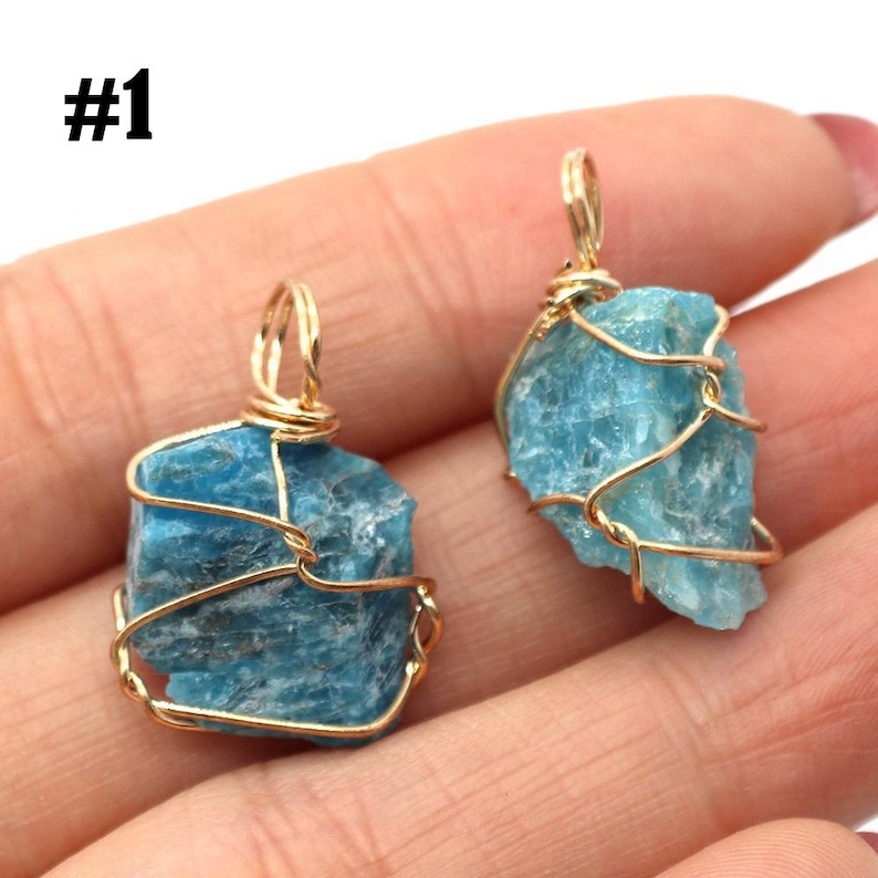 May include: Two raw, light blue apatite crystal pendants wrapped in gold-colored wire. The pendants are irregularly shaped and have a natural, textured appearance. The number "#1" is visible in the upper left corner.