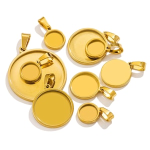 May include: A selection of gold-coloured pendant trays in different sizes. The trays are round with a flat surface for inserting a design or image. Each pendant has a loop for attaching to a chain or cord. The pendants are displayed on a white background.