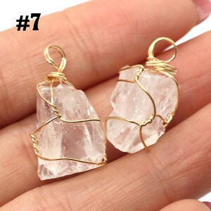 May include: Two clear quartz crystal pendants wrapped in gold-colored wire. The crystals are irregularly shaped and have a slightly translucent appearance. The wire is intricately wrapped around the crystals, forming a loop at the top for hanging. The number "#7" is in the top left corner.