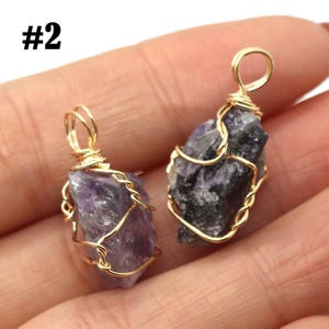 May include: Two raw amethyst pendants with gold-colored wire wrapping. The amethyst stones are a mix of purple and gray hues. Each pendant has a loop at the top for hanging. The number "#2" is in the top left corner.