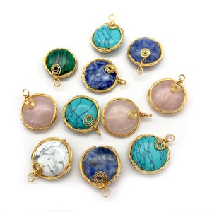 May include: A collection of gemstone pendants in various colors, including turquoise, pink, blue, green, and white. Each stone is encased in a gold-colored wire frame with a loop for hanging. The pendants are arranged on a white background.