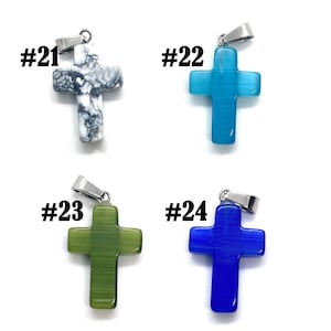 May include: Four cross pendants in various colors: white and gray, light blue, green, and dark blue. Each cross has a silver-colored bail and the numbers #21, #22, #23, and #24 are printed above each pendant. The crosses are made of a smooth, possibly stone-like material.