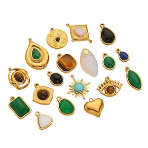 Könnte beinhalten: Eine Sammlung goldfarbener Anhänger mit verschiedenen Edelstein-Inlays. Die Anhänger weisen Formen wie Tropfen, Quadrate, Herzen und Sonnenstrahlen auf, mit Steinen in Grün, Blau, Braun und Weiß. Einige haben ein Augendesign.