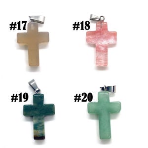 May include: Four gemstone cross pendants with silver-colored bails. The crosses are in shades of tan, pink, dark green, and light green. Each pendant is labeled with a number from #17 to #20.