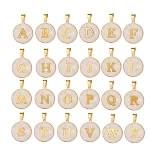Op de afbeelding: Een verzameling goudkleurige initiaalhangers. Elke hanger toont een letter van het alfabet, van A tot X, in goud tegen een witte, parelmoer achtergrond. De hangers zijn rond en hebben een gouden beugel.