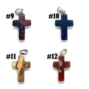 May include: Four stone cross pendants with silver-tone bails. The crosses are in various colors: brown with black spots, dark blue, tan with brown spots, and red with tan spots. Each pendant is labeled with a number.