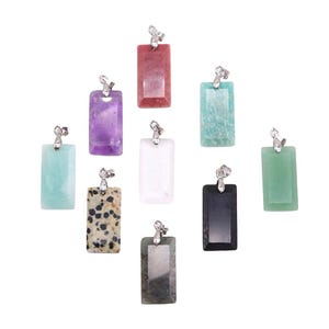 Puede incluir: Una colección de colgantes rectangulares de piedras preciosas en varios colores, incluyendo púrpura, rojo, verde y negro. Cada colgante tiene una argolla plateada para sujetarlo a una cadena. Las piedras tienen superficies pulidas.