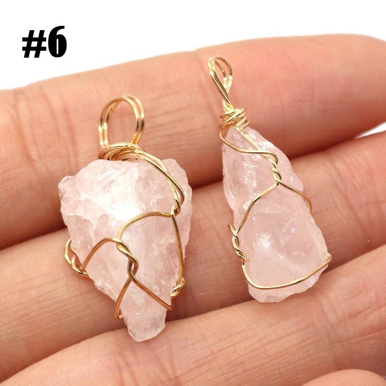 May include: Two rose quartz pendants with gold-colored wire wrapping. The raw, light pink stones are irregularly shaped and have a natural, textured appearance. The pendants are displayed against a neutral background.