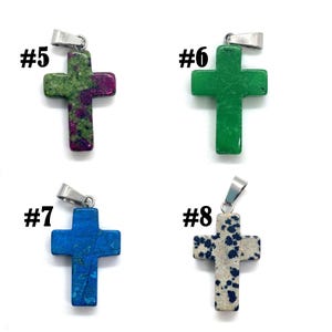 May include: Four stone cross pendants with silver-tone bails. The crosses are in shades of green, blue, and speckled beige. Each pendant is labeled with a number from #5 to #8. The crosses are likely for necklaces or other jewelry.