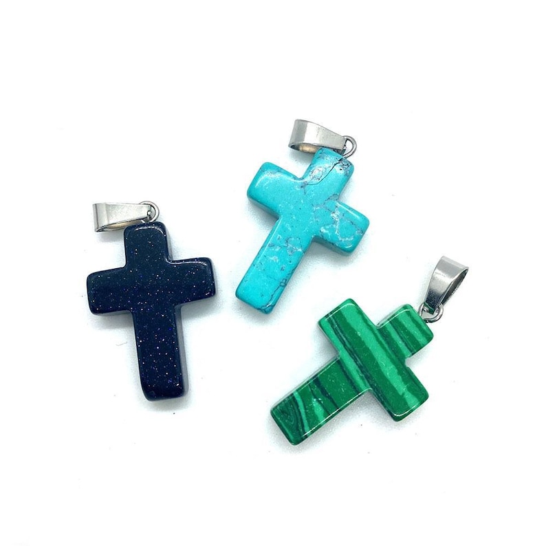 May include: Three gemstone cross pendants with silver-colored bails. One is a dark blue with glitter, another is turquoise, and the third is green with a striped pattern. These pendants are suitable for necklaces or other jewelry.