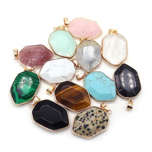Puede incluir: Una colección de colgantes de piedras preciosas en varios colores y patrones, incluyendo rosa, verde, blanco y negro. Cada colgante tiene un marco de metal dorado y un lazo para sujetarlo a una cadena o cordón.