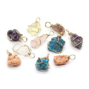 Puede incluir: Surtido de colgantes de piedras preciosas en bruto de varios colores, incluyendo morado, amarillo, rosa, azul y naranja. Cada piedra está envuelta en alambre dorado con un lazo para colgar. Se muestran sobre un fondo blanco.