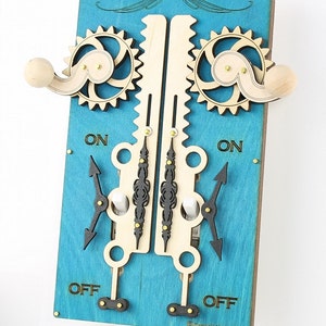 May include: A wooden light switch plate with two toggle switches. The plate is painted a bright turquoise blue and features a decorative design with gears and levers. The switches are labeled "ON" and "OFF".