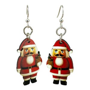 May include: A pair of Christmas-themed dangle earrings. Each earring features a wooden Santa Claus nutcracker design with a red coat, black boots, and a gold sack. The earrings hang from silver-colored hooks.