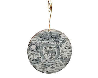 May include: A white ceramic bauble with a black and white illustration of Mackinac Island, Michigan. The ornament features a horse-drawn carriage, the Grand Hotel, Arch Rock, and the Mackinac Straits Bridge. The text "Mackinac Island" and "Michigan" are printed on the ornament.