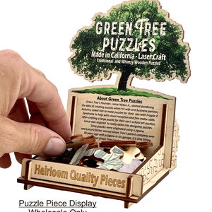 Puede incluir: Una caja de exhibici&oacute;n de madera con un rompecabezas de &aacute;rbol verde en su interior. La caja est&aacute; etiquetada como "Piezas de calidad de herencia" y "Exhibici&oacute;n de piezas de rompecabezas Venta al por mayor solamente". El rompecabezas de &aacute;rbol est&aacute; hecho por Green Tree Puzzles, que se fabrican en California utilizando la elaboraci&oacute;n con l&aacute;ser.