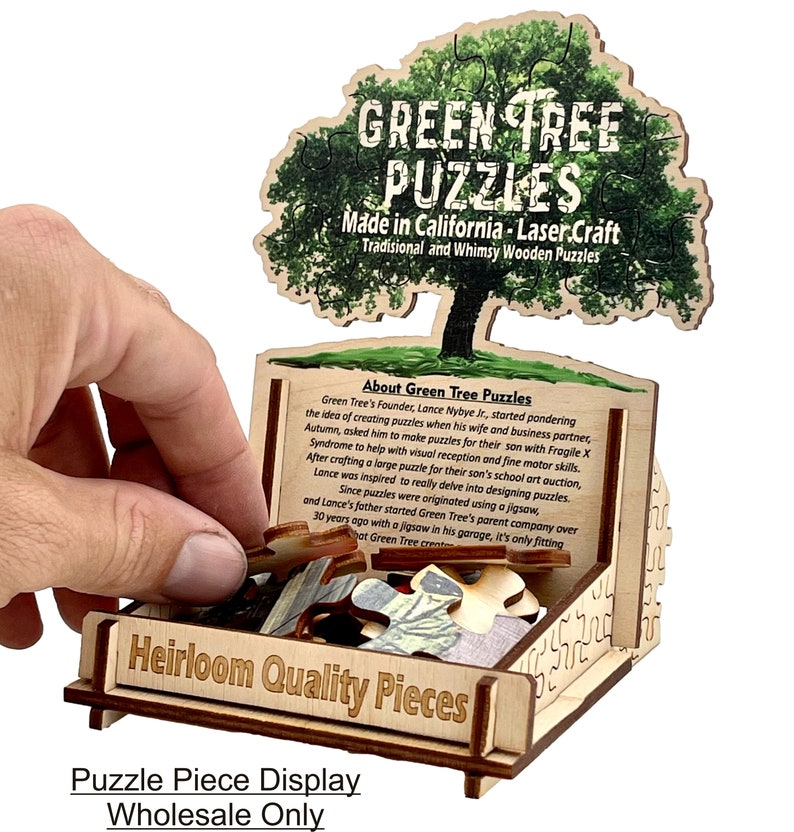 Puede incluir: Una caja de exhibici&oacute;n de madera con un rompecabezas de &aacute;rbol verde en su interior. La caja est&aacute; etiquetada como "Piezas de calidad de herencia" y "Exhibici&oacute;n de piezas de rompecabezas Venta al por mayor solamente". El rompecabezas de &aacute;rbol est&aacute; hecho por Green Tree Puzzles, que se fabrican en California utilizando la elaboraci&oacute;n con l&aacute;ser.