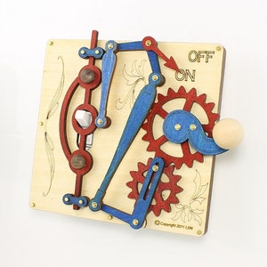 May include: A wooden light switch with a complex mechanism of gears and levers. The switch is painted in red and blue colors and has a wooden knob. The switch is labeled "ON" and "OFF".