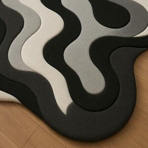 May include: A modern, abstract rug with a wavy design. The rug features a series of curved lines in shades of black, gray, and off-white. The rug is placed on a wooden floor, creating a contrast in textures and colors.