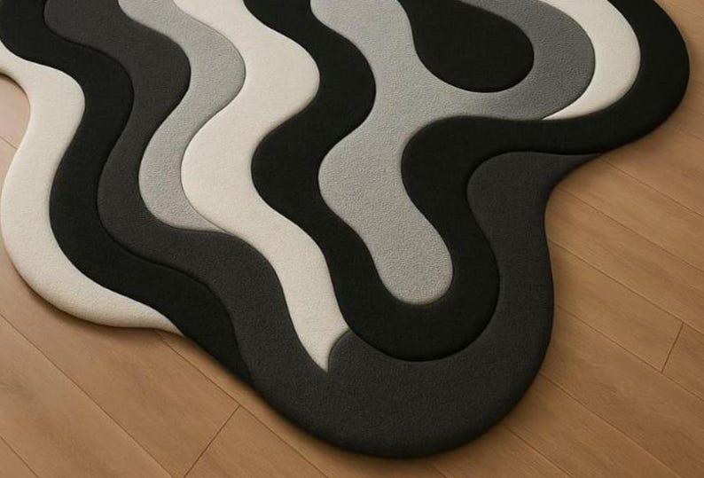 May include: A modern, abstract rug with a wavy design. The rug features a series of curved lines in shades of black, gray, and off-white. The rug is placed on a wooden floor, creating a contrast in textures and colors.