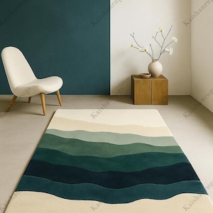 Op de afbeelding: Een rechthoekig vloerkleed met een golfpatroon in groen- en crèmetinten. Het ontwerp van het vloerkleed heeft horizontale banden in verschillende groene tinten, waardoor een gelaagd effect ontstaat. Het vloerkleed ligt op een lichtgekleurde vloer.