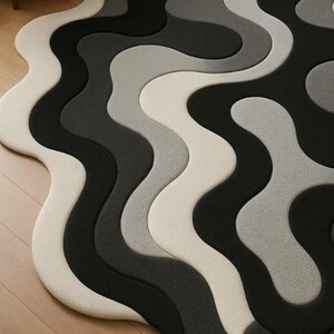 May include: A modern area rug with a wavy, abstract design. The rug features a pattern of flowing, interconnected shapes in shades of white, gray, and black. The rug's design creates a sense of movement and visual interest, suitable for contemporary home decor.