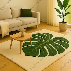 May include: A beige rug with a large green monstera leaf design. The rug is in a living room setting with a beige sofa, a small wooden table, and a potted plant. The room has a neutral color palette.