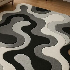 May include: A modern area rug with a wavy, abstract design. The rug features a pattern of flowing lines in shades of black, gray, and white. The rug's unique shape and color palette create a contemporary aesthetic, suitable for living rooms or bedrooms.