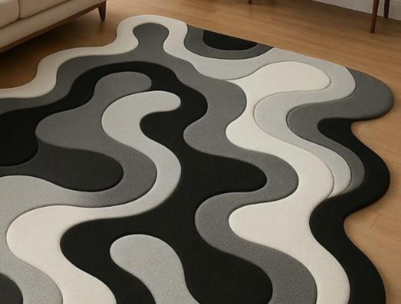 May include: A modern area rug with a wavy, abstract design. The rug features a pattern of flowing lines in shades of black, gray, and white. The rug's unique shape and color palette create a contemporary aesthetic, suitable for living rooms or bedrooms.