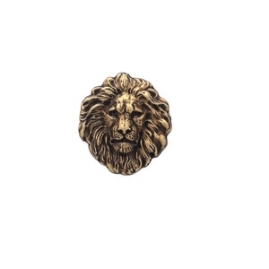 May include: A gold-colored lion head button with a detailed design. The lion's mane is textured and the face is realistic.