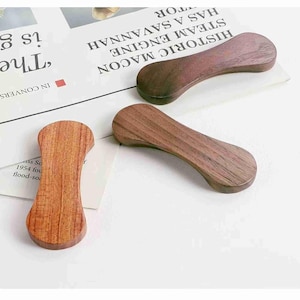 May include: Three wooden chopstick rests in varying shades of brown. The rests are curved and have a smooth, polished finish. They are arranged on a newspaper with text. The chopstick rests are a kitchen and dining accessory.