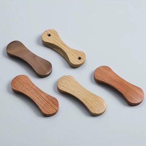 Puede incluir: Cinco reposa palillos de madera en varios tonos de marrón y beige. Cada reposa palillos tiene forma de reloj de arena redondeado, con un acabado liso y pulido. La veta de la madera es visible.