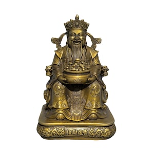 May include: A brass-coloured statue of a seated figure wearing an ornate crown and traditional robes. The figure holds a bowl filled with coins and ingots. The base features intricate relief carvings and the Chinese characters 招財進寶 in gold.
