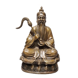 May include: A bronze-coloured statue of a seated figure with a long beard, wearing traditional robes and a headpiece. The figure holds a long-stemmed lotus flower in one hand and sits atop a base shaped like a stylised lotus blossom.