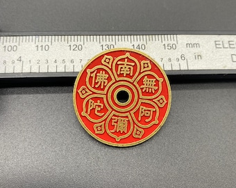 May include: A round, red and gold pendant with an intricate design and central hole. The pendant features gold lettering and symbols, with the text "南無阿彌陀佛" visible. The pendant is approximately 1.5 inches in diameter.