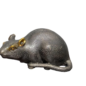 Puede incluir: Una figura de rata de metal con un acabado gris oscuro texturizado que imita el pelaje. La escultura presenta detalles dorados pulidos en las orejas y alrededor de los ojos, mostrando a la rata en posición agachada con la cola enroscada.