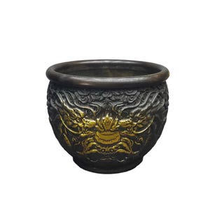 May include: A dark brown, rounded metal bowl featuring intricate, raised relief carvings of two dragons facing each other. The dragon figures are highlighted with a metallic gold finish, contrasting against the dark, textured background of the vessel.